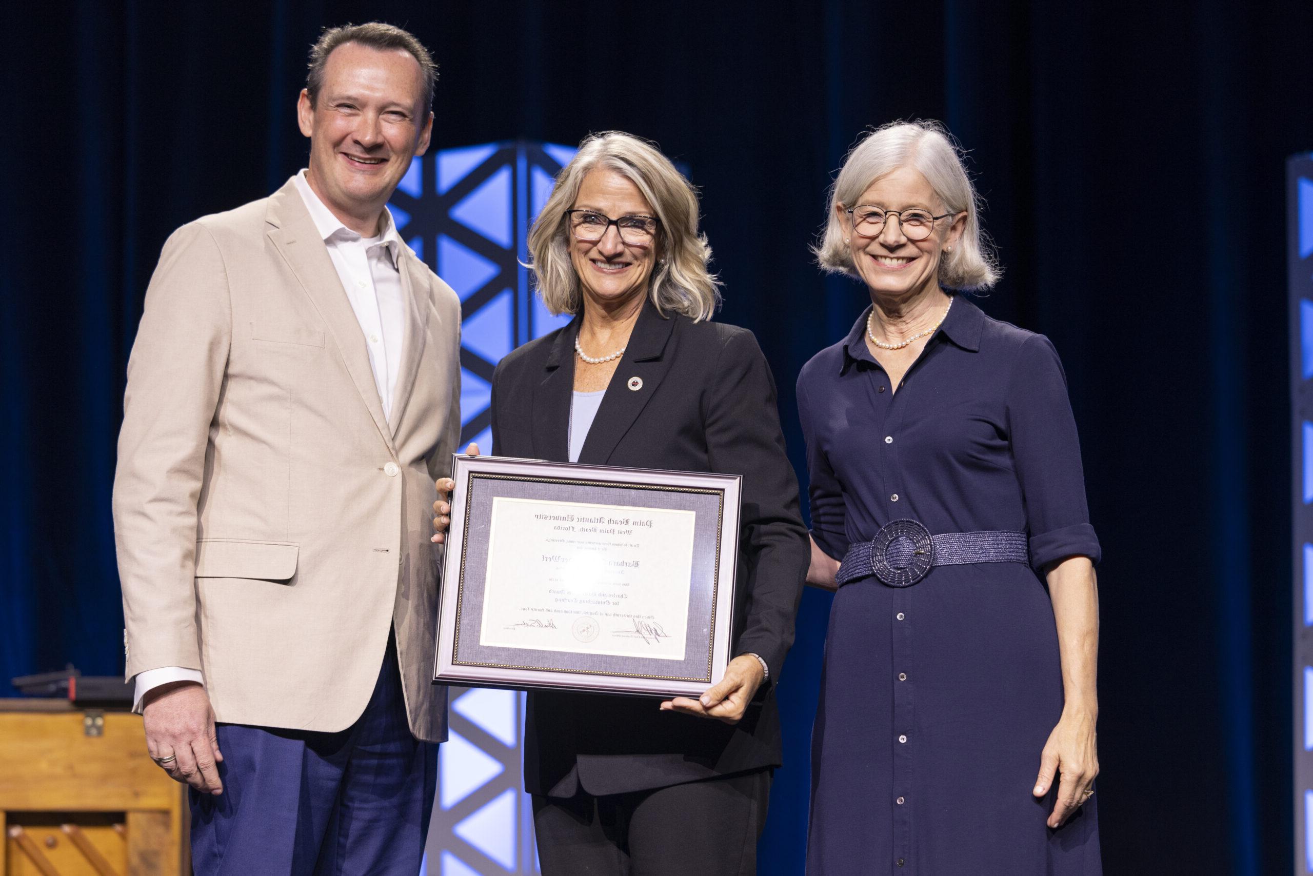 Barbara VanderWerf smiling and holding her award on stage